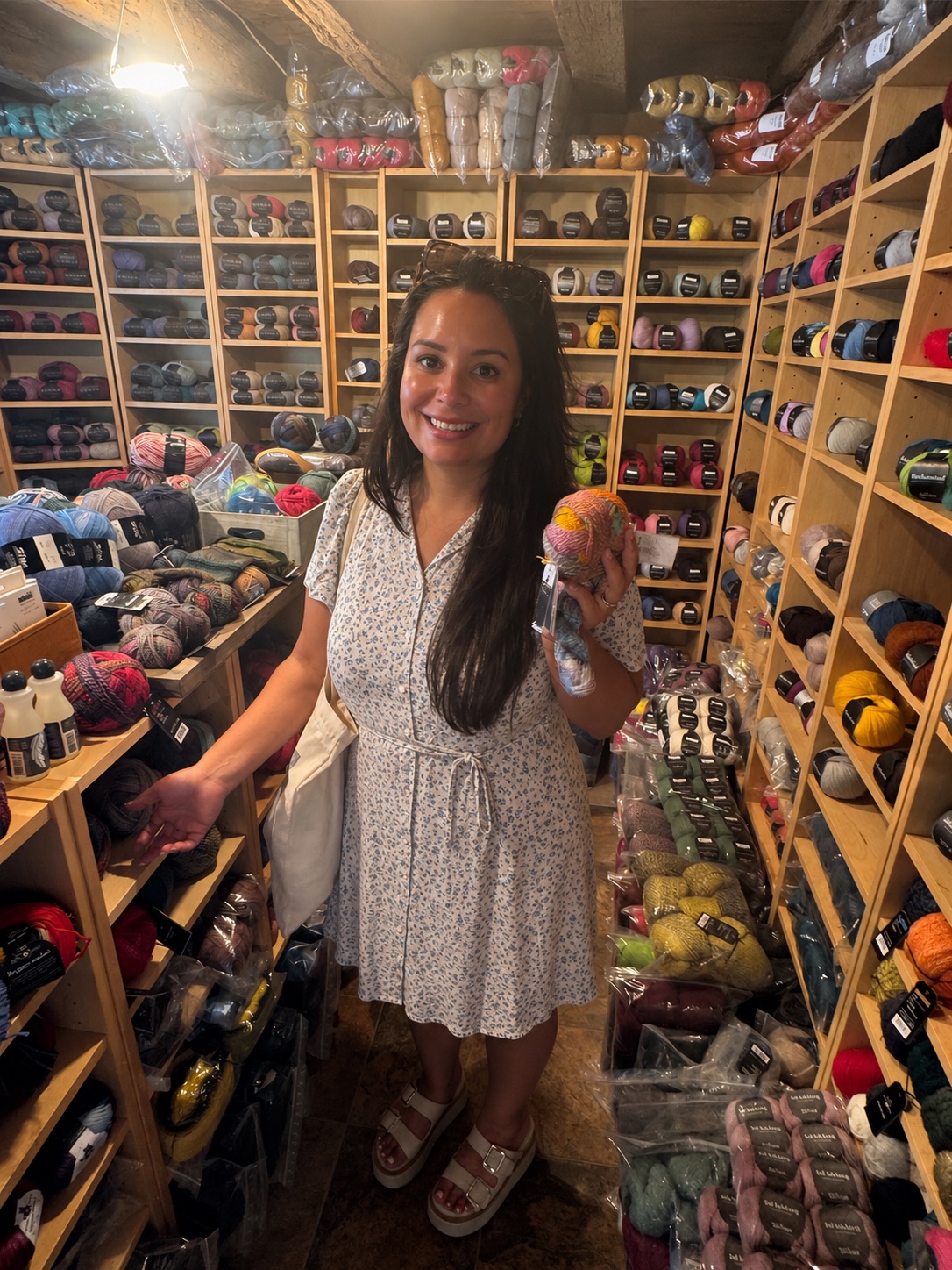 Angelica Lemke smiling and holding colorful yarn in front of a wall of yarn skeins.